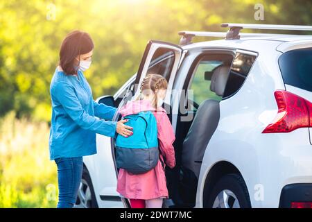 Madre che mette la figlia in auto dopo le classi durante l'epidemia di coronavirus Foto Stock