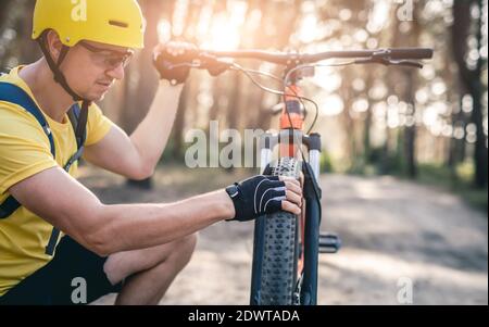 Uomo che controlla la pressione degli pneumatici sulla ruota della bicicletta durante la guida foresta Foto Stock