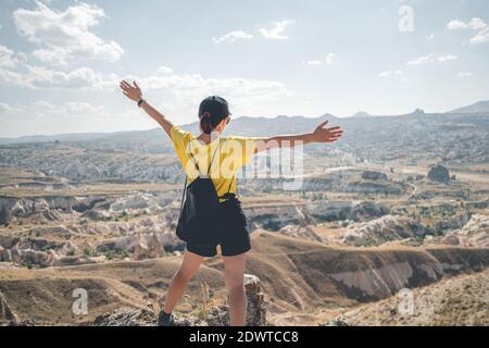 Donna turistica con zaino in piedi indietro sulla cima della montagna in Cappadocia a braccia aperte, Turchia Foto Stock