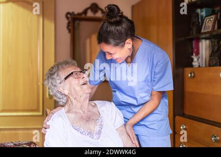 Donna anziana felice che ride con il suo caregiver a casa. Concetto di assistenza domestica senior. Foto Stock