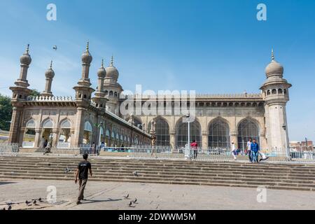 Pellegrini musulmani che camminano nella moschea Mecca Masjid contro il cielo blu e colombe che volano in cielo, un famoso monumento a Hyderabad Foto Stock