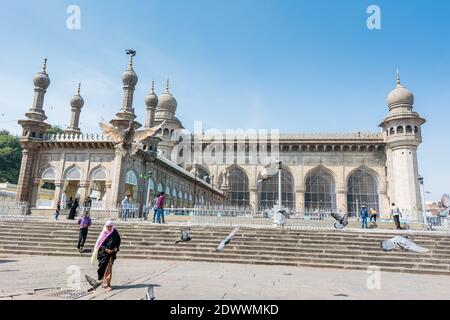 Pellegrini musulmani che camminano nella moschea Mecca Masjid contro il cielo blu e colombe che volano in cielo, un famoso monumento a Hyderabad Foto Stock