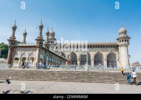 Pellegrini musulmani che camminano nella moschea Mecca Masjid contro il cielo blu e colombe che volano in cielo, un famoso monumento a Hyderabad Foto Stock