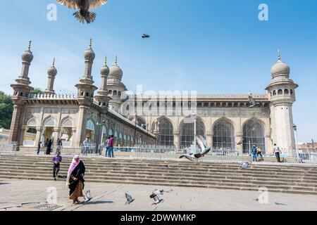 Pellegrini musulmani che camminano nella moschea Mecca Masjid contro il cielo blu e colombe che volano in cielo, un famoso monumento a Hyderabad Foto Stock