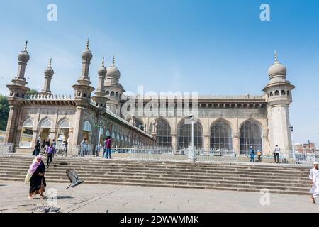 Pellegrini musulmani che camminano nella moschea Mecca Masjid contro il cielo blu e colombe che volano in cielo, un famoso monumento a Hyderabad Foto Stock