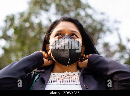 Primo piano di una donna d'affari latina che indossa una maschera facciale per motivi di protezione durante la pandemia del covid 19. Sta mettendo su una maschera Foto Stock