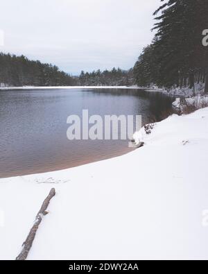 Alba su una mattina invernale sovrastata dopo una nevicata vicino ad un lago. La sabbia arancione si staglia contro il cielo blu e l'acqua blu. Foto Stock