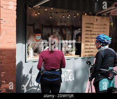 Due Signore che ordinano caffè dalla vetrina in un contenitore con protezione in plexiglas, da giovane uomo con maschera a Ottawa Foto Stock