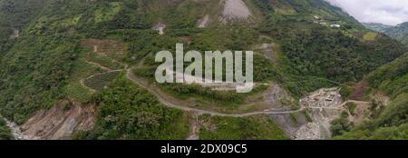 Strade e deforestazione sul versante montano sopra una valle del fiume andino con un impianto idroelettrico a destra. Vicino a Banos, Ecuador Foto Stock