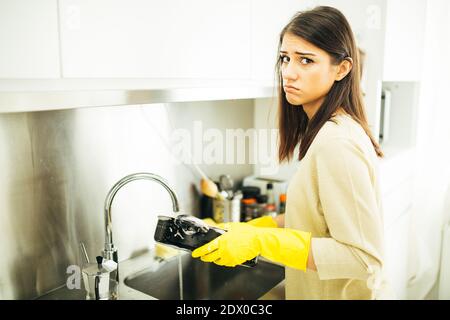 Donna stanca di lavarsi a mano e di pulizia chores.Housewife donna lavare piatti in cucina. Lavare le piastre manualmente, indossando la gomma gialla di pulizia glo Foto Stock