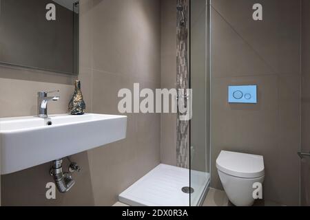 Moderno interno grigio di un piccolo bagno con doccia in vetro, specchio rettangolare, wc montato, lavabo bianco appeso Foto Stock