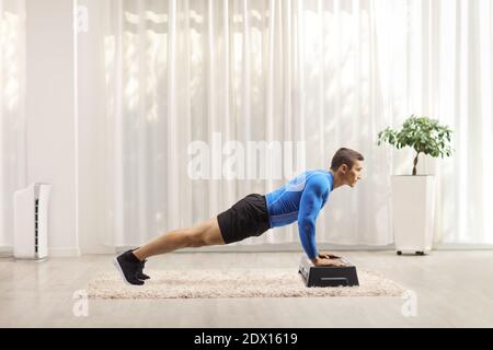 Giovane uomo che esercita i push-up su una piattaforma aerobica di punto a. casa Foto Stock