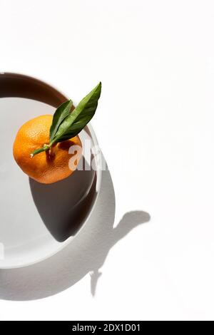 Mandarino o arancio, clementina, agrumi con foglie verdi su piastra grigia su sfondo bianco. Mandarino succoso maturo con foglie. Vista dall'alto. Foto Stock