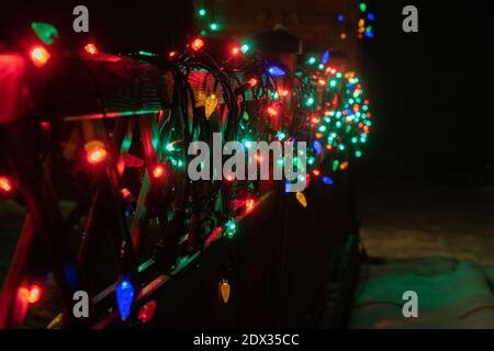 Vere luci di Natale sfocate multicolore su recinzione in legno terrazza. Molte lampade lampeggianti che cambiano colore in sequenza. Capodanno e decorazione di Natale Foto Stock