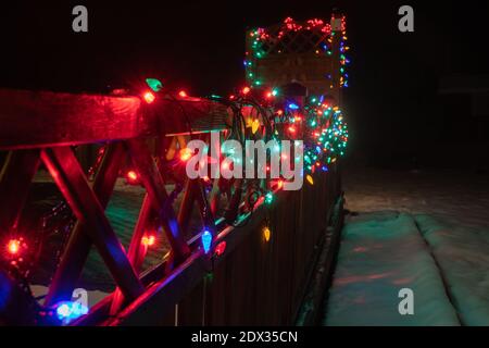 Vista prospettica delle luci multicolore di Natale sfocate su recinzione in legno. Molte lampade lampeggianti che cambiano colore in sequenza. Anno nuovo A. Foto Stock