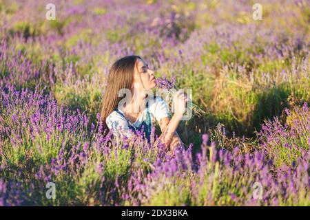 Giovane bella ragazza si siede su un prato di lavanda con un bouquet di fiori nelle loro mani Foto Stock