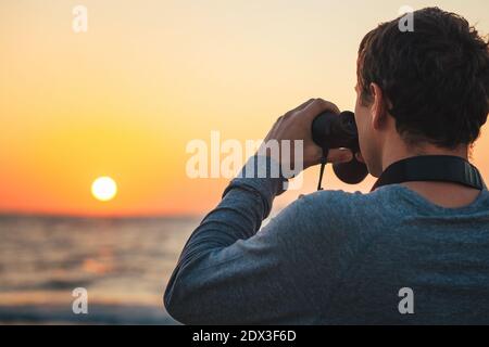 Un uomo con binocoli in mano sulla costa del mare durante il tramonto Foto Stock