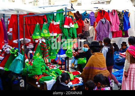 23 dicembre 2020, LA Paz, BOLIVIA: Una donna di Aymara o colita che indossa abiti tradizionali per lo shopping in una bancarella di strada che vende cappelli e costumi di Natale di padre e Grinch in un mercato di Natale. Foto Stock