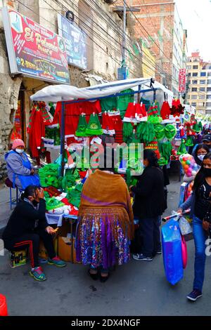 23 dicembre 2020, LA Paz, BOLIVIA: Una donna di Aymara o colita che indossa abiti tradizionali per lo shopping in una bancarella di strada che vende cappelli e costumi di Natale di padre e Grinch in un mercato di Natale. Foto Stock