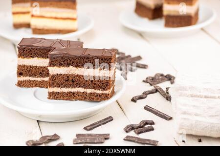 Torta al cioccolato con tre impasti al cioccolato e due pavimenti in crema. Dessert ideale per matrimoni e feste. Deliziosa torta servita su un tavolo di legno bianco. Foto Stock