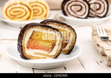 Punch dessert svizzero a rotolo con guarnizione al cioccolato. Sullo sfondo altri due tipi di roulades. Il Roulade è una tradizionale torta servita in occasione di matrimoni. Foto Stock