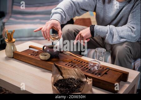 La tradizione cinese del tè bere da vicino. La mano di un uomo tiene una teiera fatta di argilla Yixing e versa il delizioso tè in tazze Foto Stock