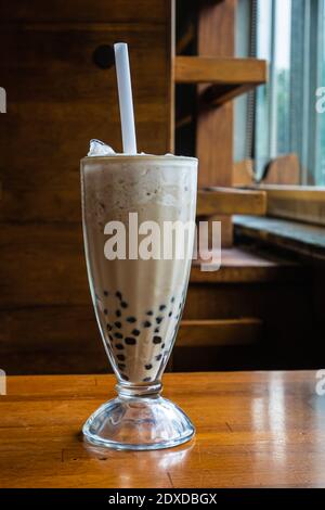 Primo piano della tradizionale bevanda a base di tè al latte a bolle taiwanese, bevanda fredda taiwanese su classico tavolo in legno. Foto Stock