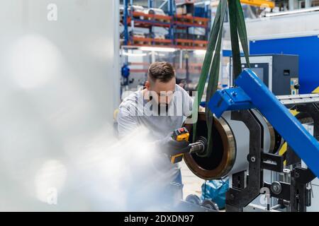 Lavoratore manuale maschio che esamina la parte di macchina di acciaio nell'industria illuminata Foto Stock