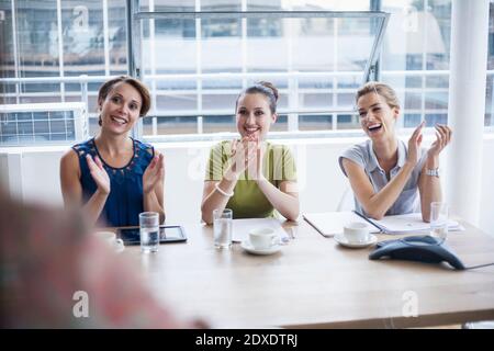 Le colleghe applaudono mentre si siedono nella sala riunioni durante la riunione in ufficio Foto Stock