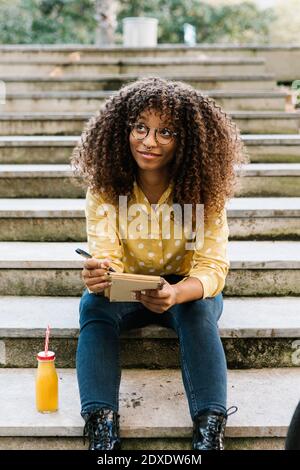 Donna premurosa con libro che guarda in su mentre si siede sui gradini Foto Stock
