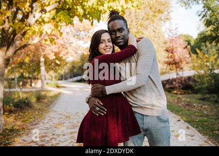 Donna incinta sorridente che abbraccia l'uomo mentre si trova sul sentiero dentro parcheggio Foto Stock