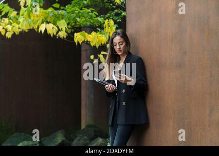 Bella donna d'affari che indossa occhiali utilizzando il telefono cellulare contro la parete marrone Foto Stock