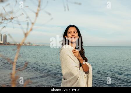 Sorridente donna pensierosa che guarda via mentre si sta in piedi sull'acqua a. spiaggia Foto Stock