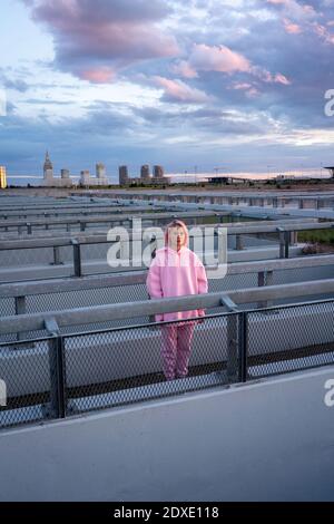 Giovane donna con capelli rosa che indossa una camicia con cappuccio rosa in piedi ringhiera Foto Stock