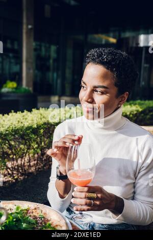 Sorridente giorno di lavoro sognando mentre beve succo al ristorante durante giorno di sole Foto Stock