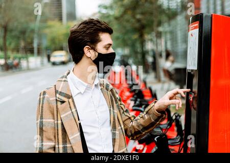 Giovane uomo in maschera noleggio biciclette in città Foto Stock