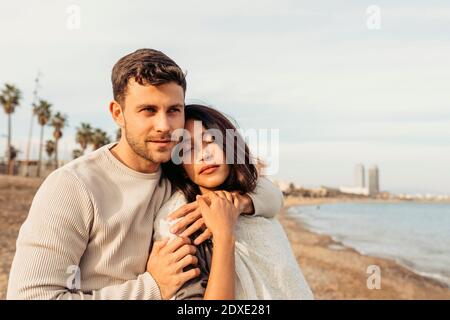 Fidanzato abbracciando la ragazza mentre si alza contro il cielo sulla spiaggia Foto Stock