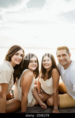 Famiglia sorridente seduta sul molo contro il cielo Foto Stock
