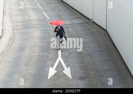 Uomo d'affari con ombrello rosso che cammina sulla segnaletica stradale Foto Stock