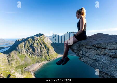 Donna che guarda la vista mentre si siede sulla montagna a Ryten, Lofoten, Norvegia Foto Stock