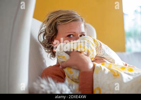 Donna che copre la faccia con coperta mentre si siede sul divano a. casa Foto Stock