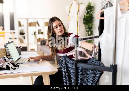Giovane uomo d'affari con un computer portatile che guarda i top disposti su rack in studio Foto Stock