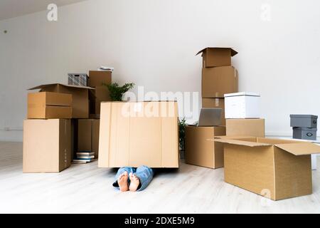 Giovane uomo coperto all'interno di scatola di cartone sdraiato in nuovo appartamento Foto Stock