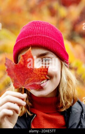 Adolescente ragazza che indossa cappello a maglia che tiene la foglia d'acero all'aperto Foto Stock