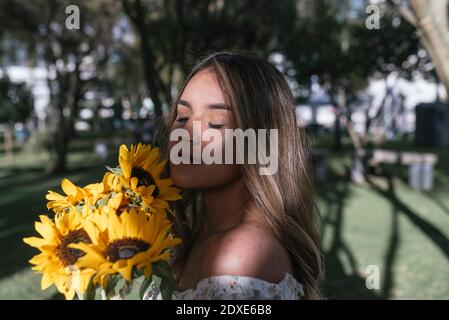 Giovane donna con gli occhi chiusi che odorano girasoli sul cortile posteriore Foto Stock