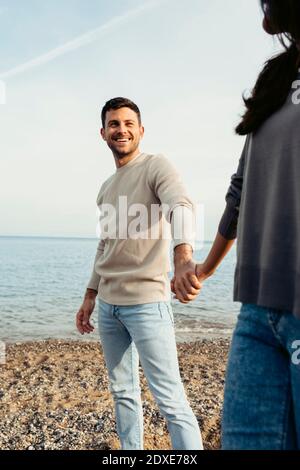 Uomo sorridente che tiene la mano della donna mentre si trova in spiaggia Foto Stock