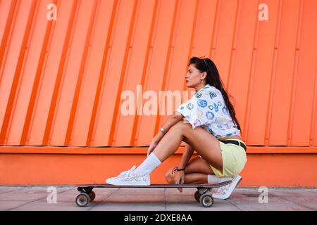 Ritratto di bella ragazza accovacciata accanto a longboard di fronte parete di ferro corrugata Foto Stock