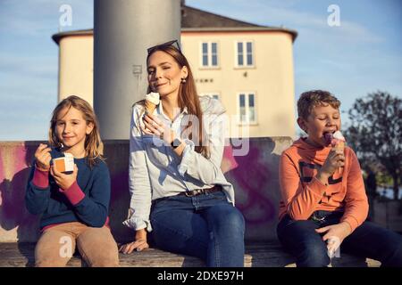 Madre che ha gelato con i bambini mentre si siede sulla panca Foto Stock