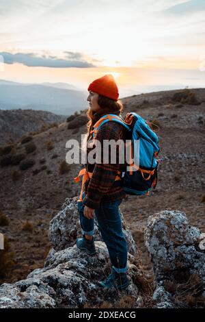 Donna che si guarda lontano mentre si è in piedi sulla montagna rocciosa durante il tramonto Foto Stock