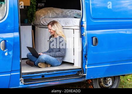 Donna con capelli biondi che lavora su un computer portatile in casa a motore Foto Stock